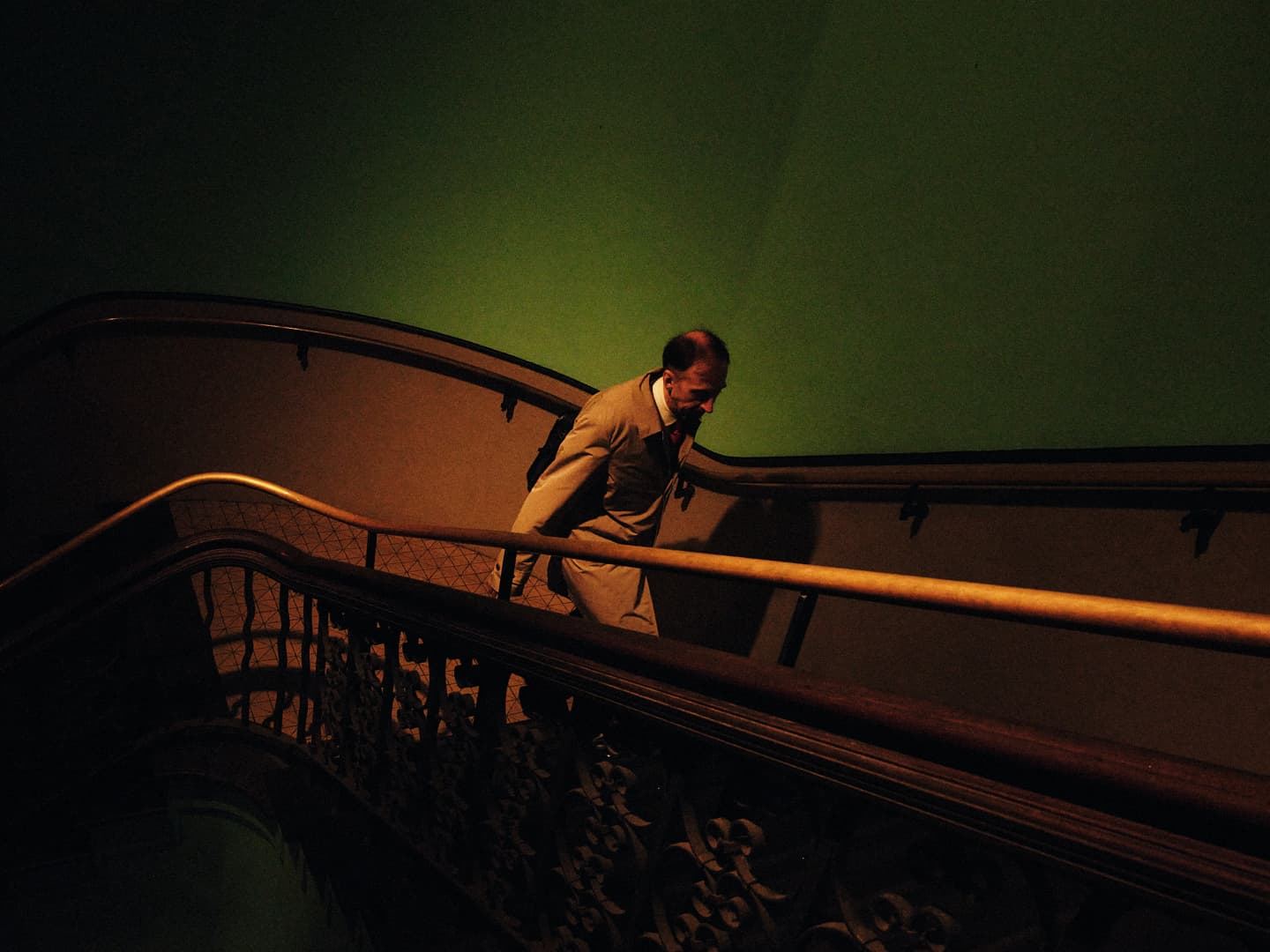 Man ascending staircase, green wall, warm light